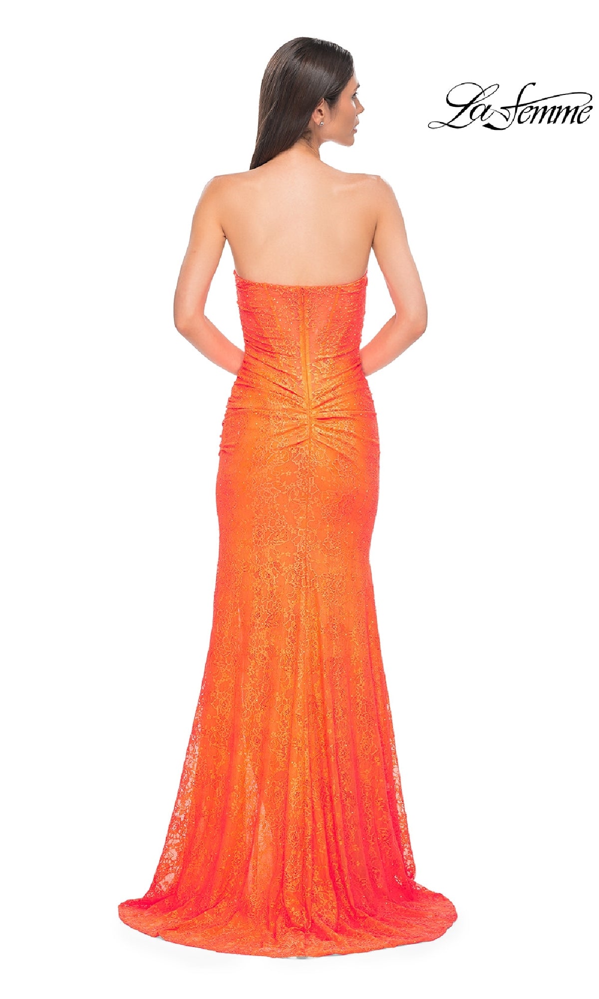 A woman with long brown hair models the La Femme 32773 Strapless Long Beaded Prom Dress in vibrant orange, featuring a floor-length design and slight train. The photo shows her from the back with the